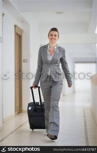 Happy business woman walking with bag on wheels