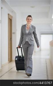Happy business woman walking with bag on wheels