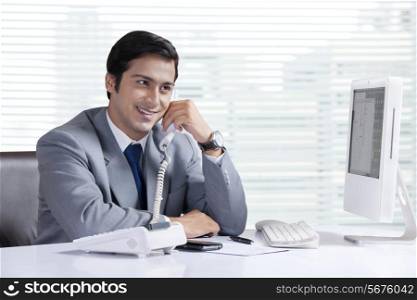 Happy businessman answering telephone at office desk