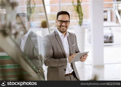 Happy businessman dressed in suit standing  in modern office  and using tablet