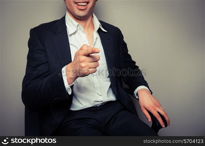Happy businessman is sitting in an office chair and is laughing and pointing