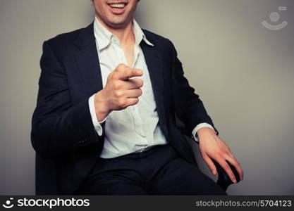 Happy businessman is sitting in an office chair and is laughing and pointing