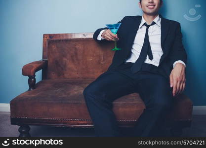 Happy businessman relaxing on sofa with cocktail