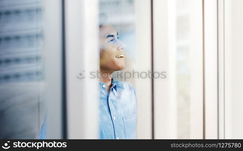 Happy Businessman Standing by the Window in Office. Looking away and Smiling. Dreaming for Success. Snap from Outside Building