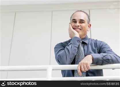 Happy businessman standing in hallway. Portrait of smiling proud business man standing in office hallway leaning on railing with copy space