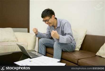 Happy businessman using laptop with documents in living room