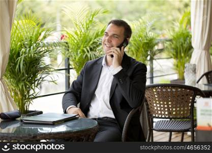 Happy businessman using mobile phone at outdoor summer restaurant