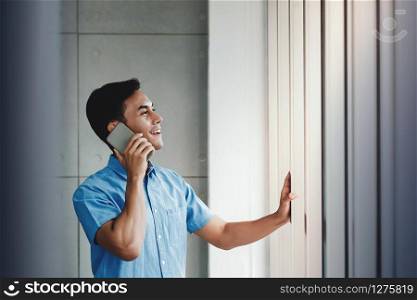 Happy Businessman Using Smartphone and Standing by the Window in Office. Talking with someone via Mobile Phone. Looking Outside