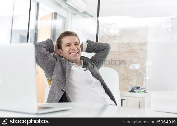 Happy businessman with hands behind head sitting at desk