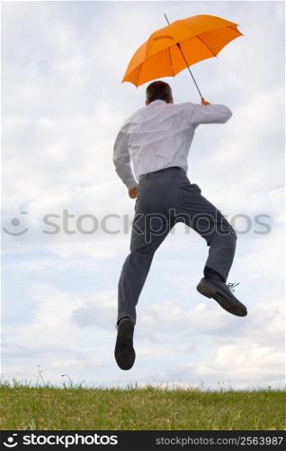 Happy businessman with orange umbrella jumping in a meadow