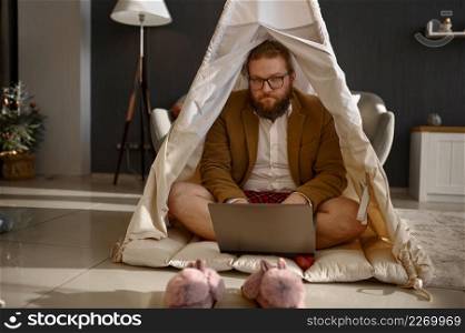 Happy businessman working laptop in home teepee tent. Happy male relaxing, work on weekend. Happy businessman working laptop in home tent