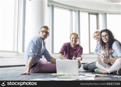 Happy businesspeople looking away while working on floor at creative office