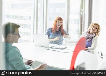 Happy businesspeople sitting at desk in creative office