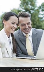 Happy businesspeople using laptop outdoors