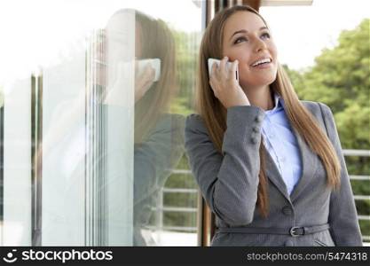 Happy businesswoman answering cell phone by glass door
