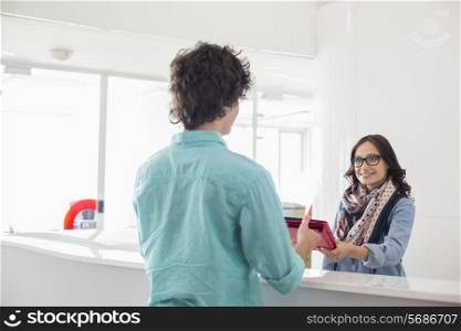 Happy businesswoman giving files to male colleague at counter in creative office