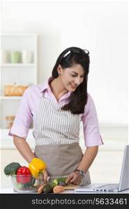 Happy businesswoman looking at laptop while cooking in kitchen