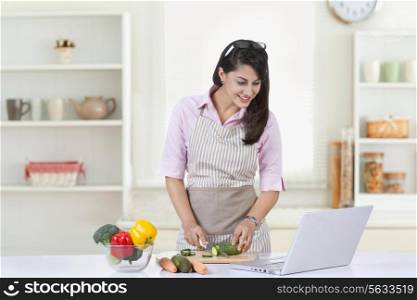 Happy businesswoman looking at laptop while preparing food in kitchen