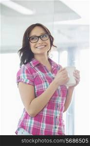 Happy businesswoman looking away while holding coffee mug in creative office