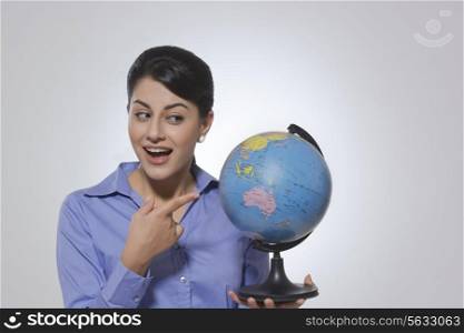 Happy businesswoman pointing at globe against gray background