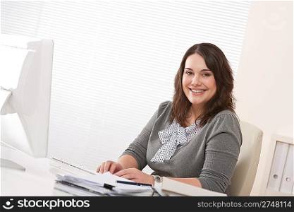 Happy businesswoman sitting at office desk with computer