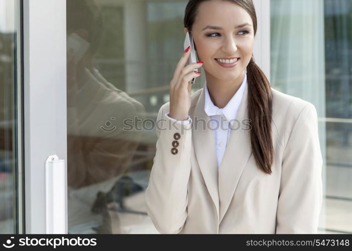 Happy businesswoman using cell phone by glass door