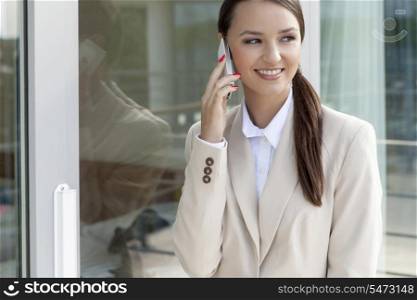 Happy businesswoman using cell phone by glass door