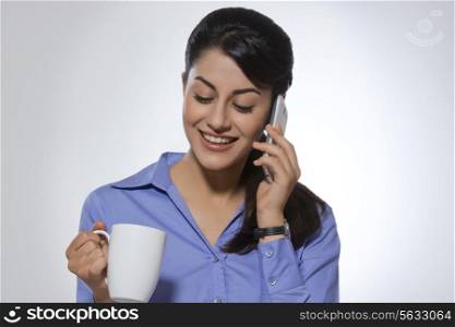 Happy businesswoman using phone while having coffee against gray background
