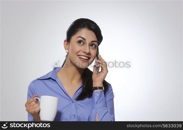 Happy businesswoman with coffee mug answering phone over gray background