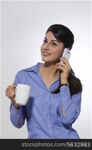 Happy businesswoman with coffee mug using phone over gray background