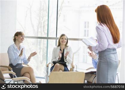 Happy businesswomen clapping for colleague after presentation in office