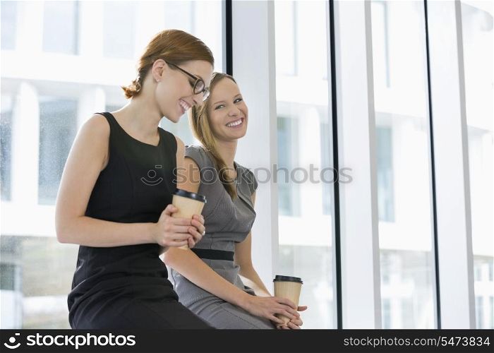 Happy businesswomen with disposable coffee cups at office