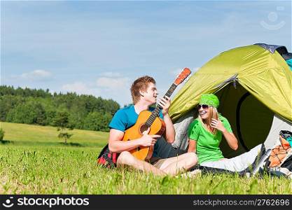 Happy camping couple sitting by tent play guitar sunny countryside