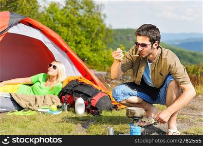 Happy camping couple with tent backpack cooking in sunny countryside