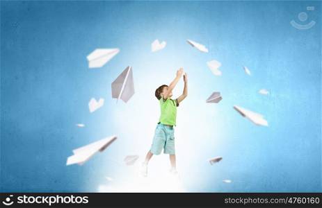 Happy careless childhood. Little cute boy catching paper airplane on colorful background
