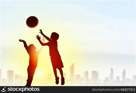 Happy careless childhood. Silhouettes of children jumping to catch ball on sunset background
