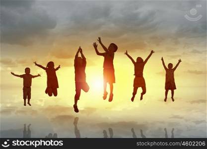 Happy careless childhood. Silhouettes of group of children jumping high joyfully on sunrise background