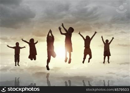 Happy careless childhood. Silhouettes of group of children jumping high joyfully on sunset background