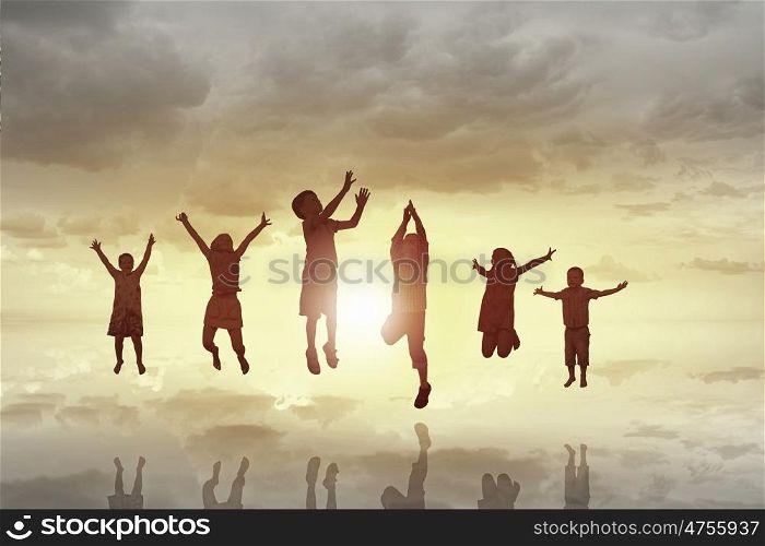 Happy careless childhood. Silhouettes of group of children jumping high joyfully on sunset background