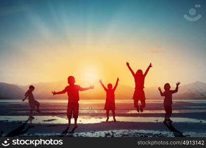 Happy careless childhood. Silhouettes of group of children jumping high joyfully on sunset background