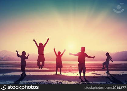 Happy careless childhood. Silhouettes of group of children jumping high joyfully on sunset background