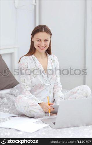Happy casual beautiful woman working on a laptop sitting on the bed in the house. woman checking social apps and working. Communication and technology concept. Woman in quarantine for Coronavirus.. Happy casual beautiful woman working on a laptop sitting on the bed in the house. woman checking social apps and working. Communication and technology concept. Woman in quarantine for Coronavirus