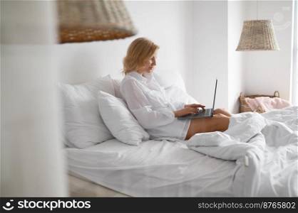 Happy casual beautiful woman working on laptop sitting on bed at home. Online job, remote education, blogging or shopping on internet. Woman working on laptop sitting on bed at home