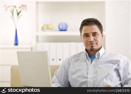 Happy casual man teleworking using laptop computer at home.