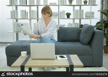 Happy Caucasian senior woman is relaxing , reading newspaper in living room