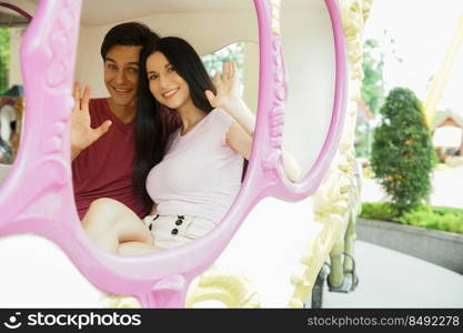 Happy Caucasian young couples smile and look at camera on merry go round at the amusement park