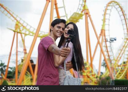 Happy Caucasian young couples take camera selfie photos together at theme park roller coaster on background 