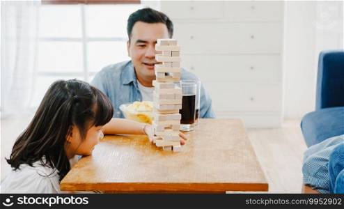 Happy cheerful Asia family having fun play board game hobby with wooden tower at sofa couch in living room at home. Spending time together, Social distancing, Quarantine for corona virus prevention.