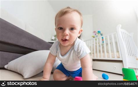 Happy cheerful baby boy playing on floor and looking at camera