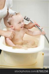 Happy cheerful baby boy playing with shower head in bath